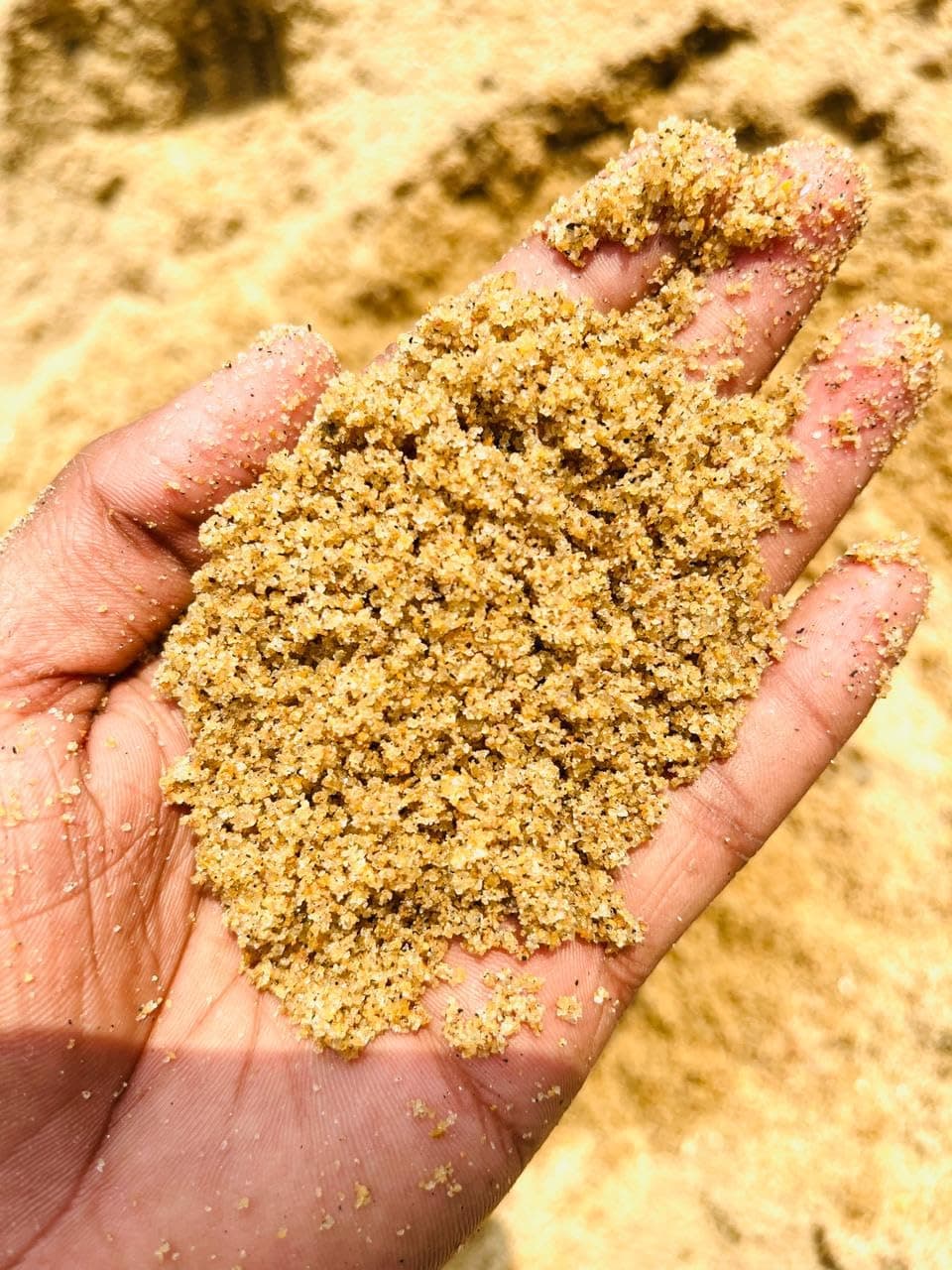 A hand holding a fistful of golden sand at the materials yard